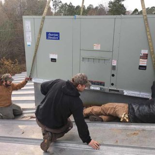 The technicians installing a rooftop AC unit on commercial building